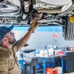 Professional,Caucasian,Mechanic,Standing,Under,The,Vehicle,Lifted,On,Car